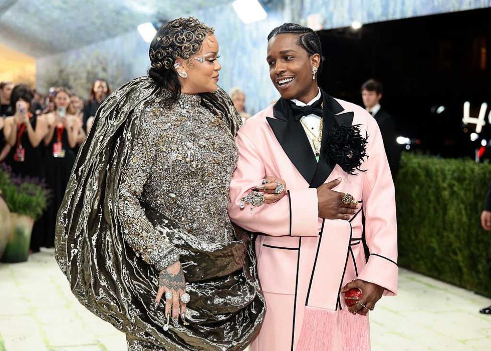 Two people in ornate outfits walking arm in arm at a glamorous event.