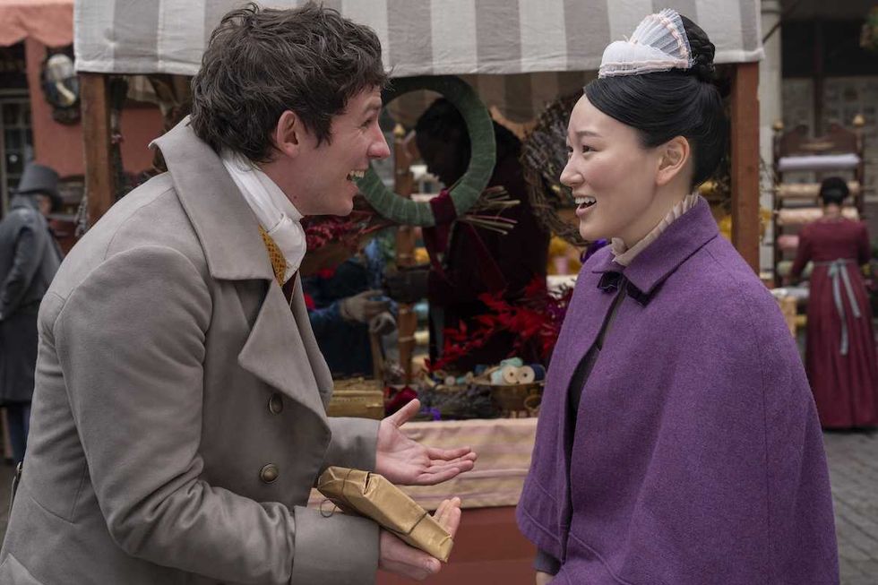 Two people in period clothing conversing happily at an outdoor market stall.
