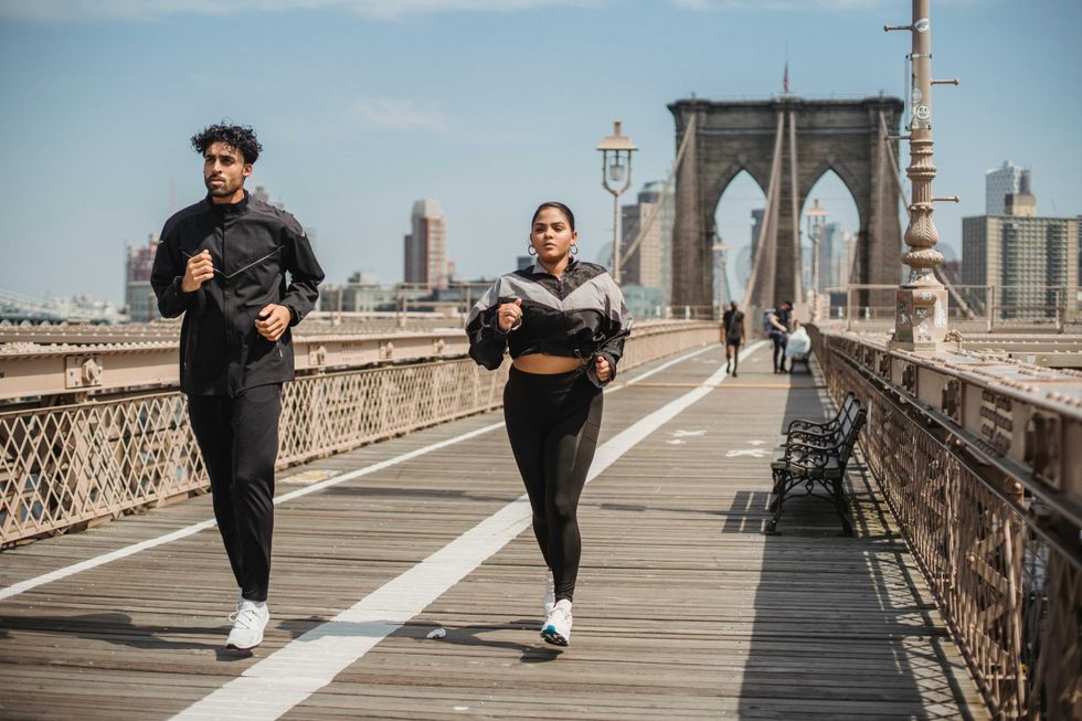Two people jogging on the Brooklyn Bridge under a clear sky.