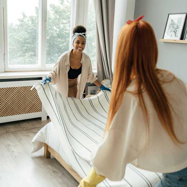 Two people making a bed near a window with a striped bedspread.