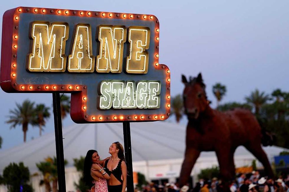 Two people pose under a lit "Mane Stage" sign with a horse statue in the background.