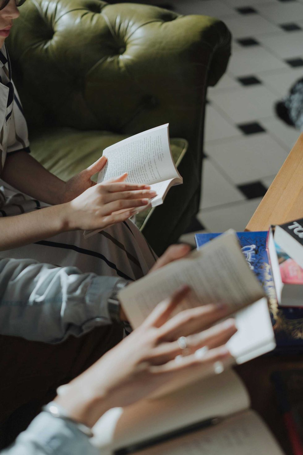 Two people reading books on a green couch with more books on a wooden table nearby.