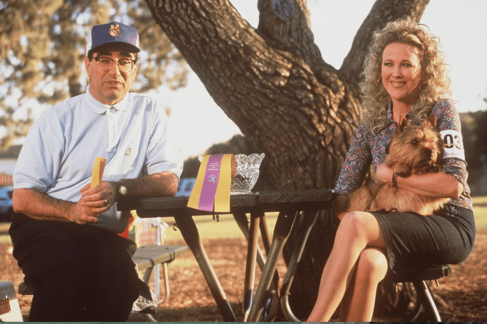 Two people sitting at a park table with a small dog and a trophy.