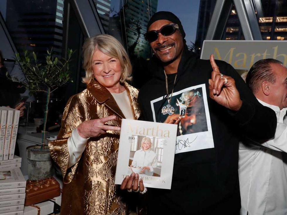 Two people smiling and holding a magazine at an event, with books in the background.