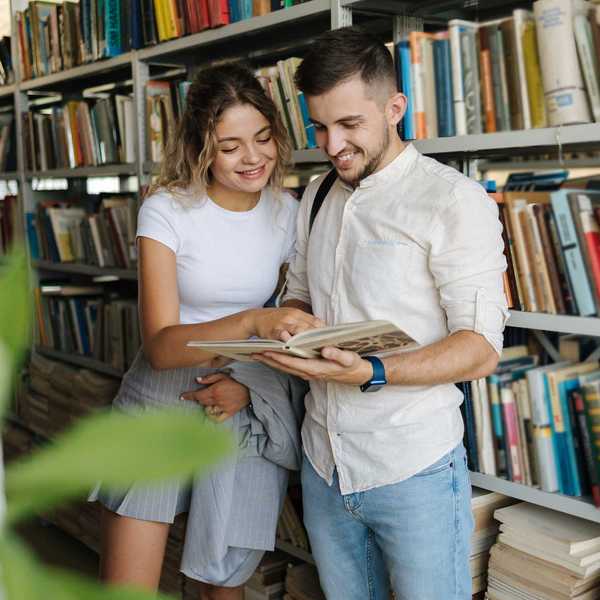 Two people smiling and reading a book in a library.