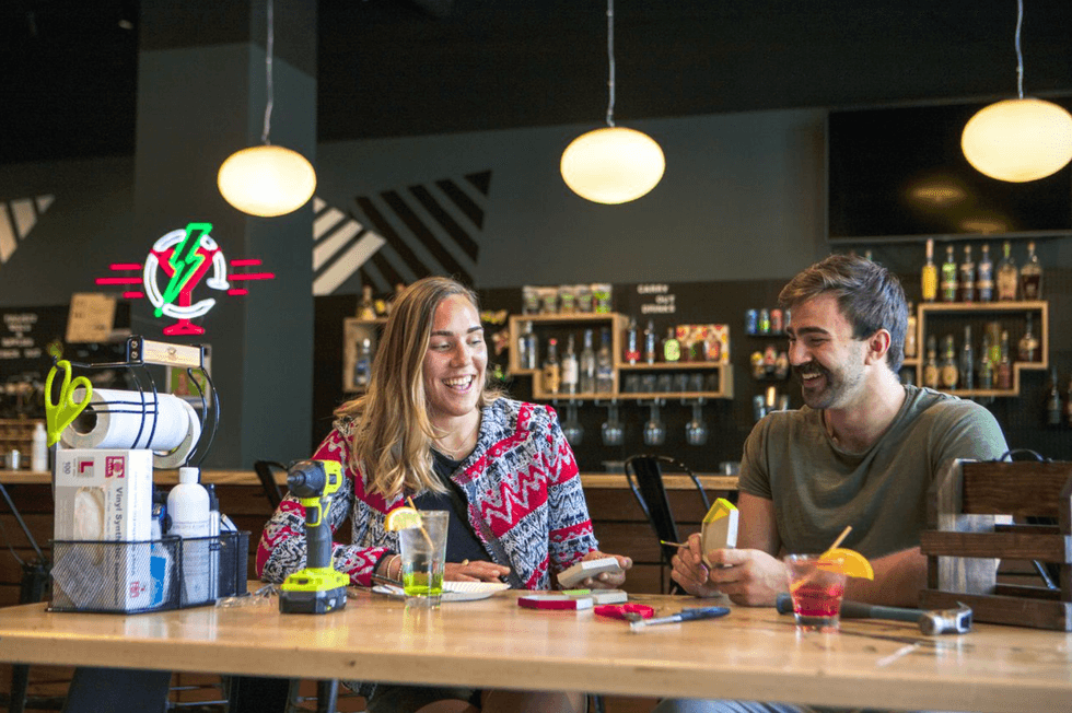 Two people smiling at a table with drinks in a lively bar setting.