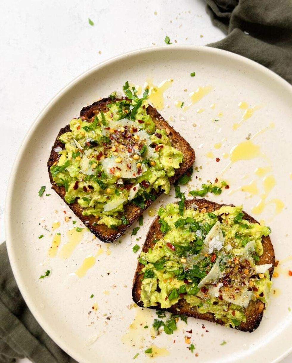 Two pieces of avocado toast sit on a white plate.