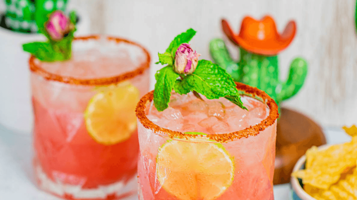 Two pink cocktails with lime slices, mint, and spicy rims next to lime and chips.