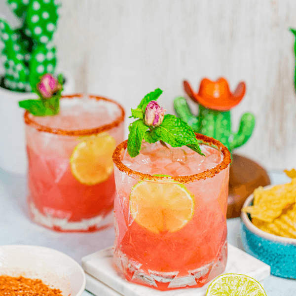 Two pink cocktails with lime slices, mint, and spicy rims next to lime and chips.