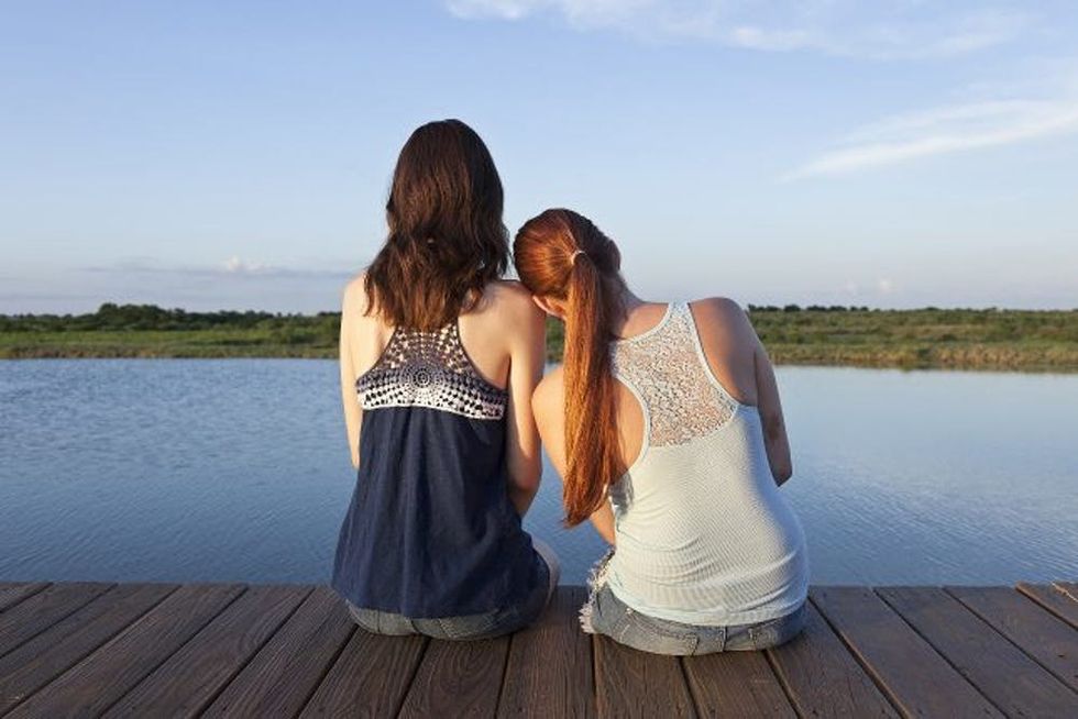 Two sisters sit together on a dock watching a lake