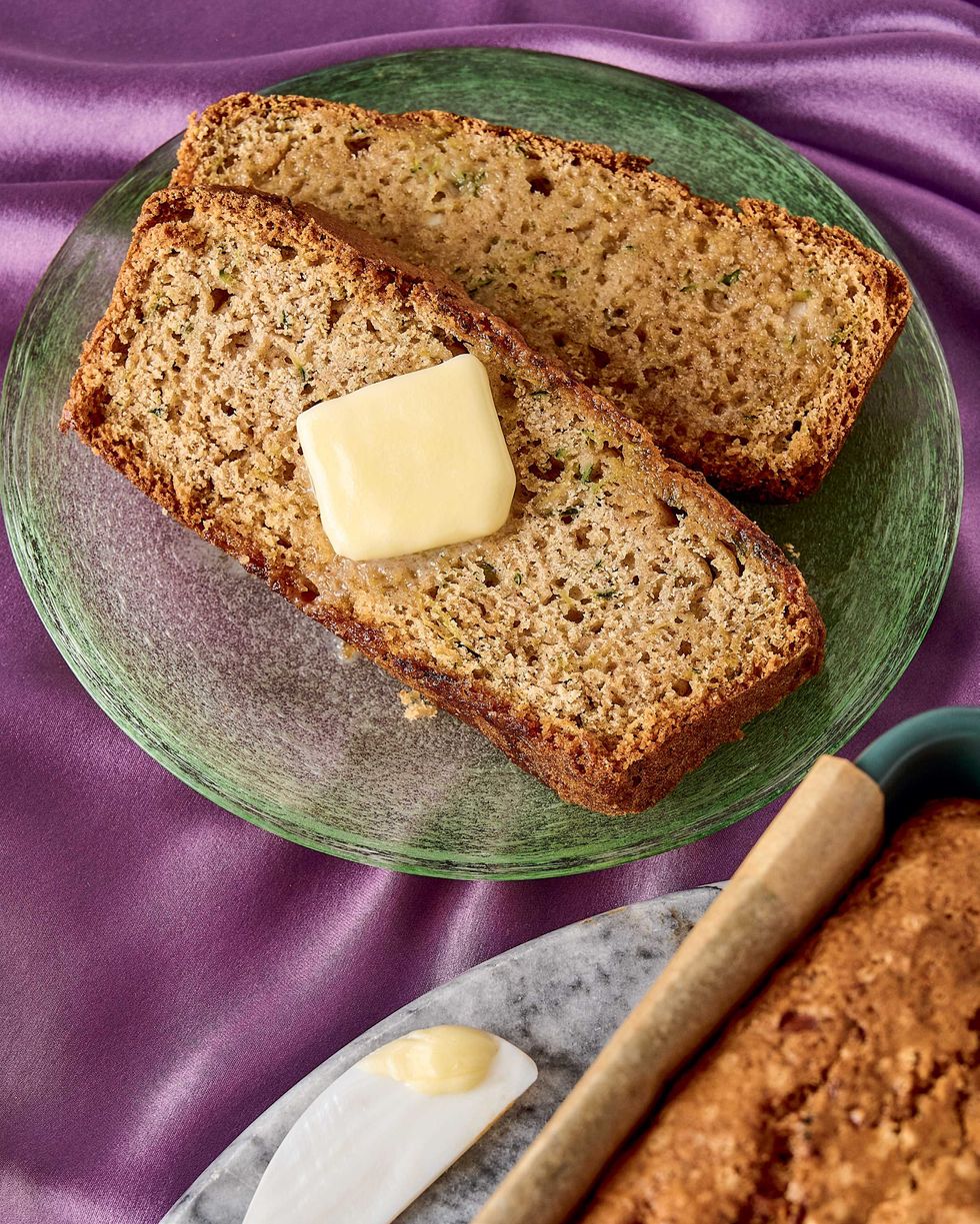 Two slices of zucchini bread on a green plate, one topped with a pat of butter.