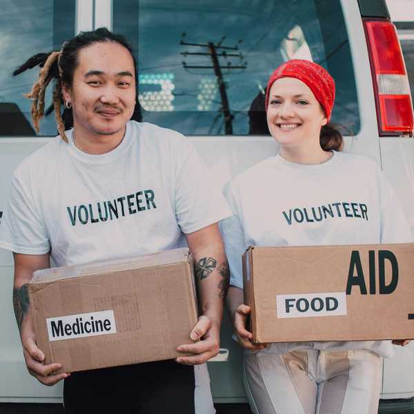 Two volunteers holding boxes labeled "Medicine" and "Food" near a vehicle.