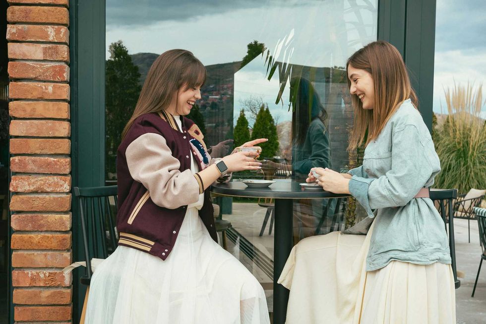 Two women chatting and laughing over coffee at an outdoor cafe.