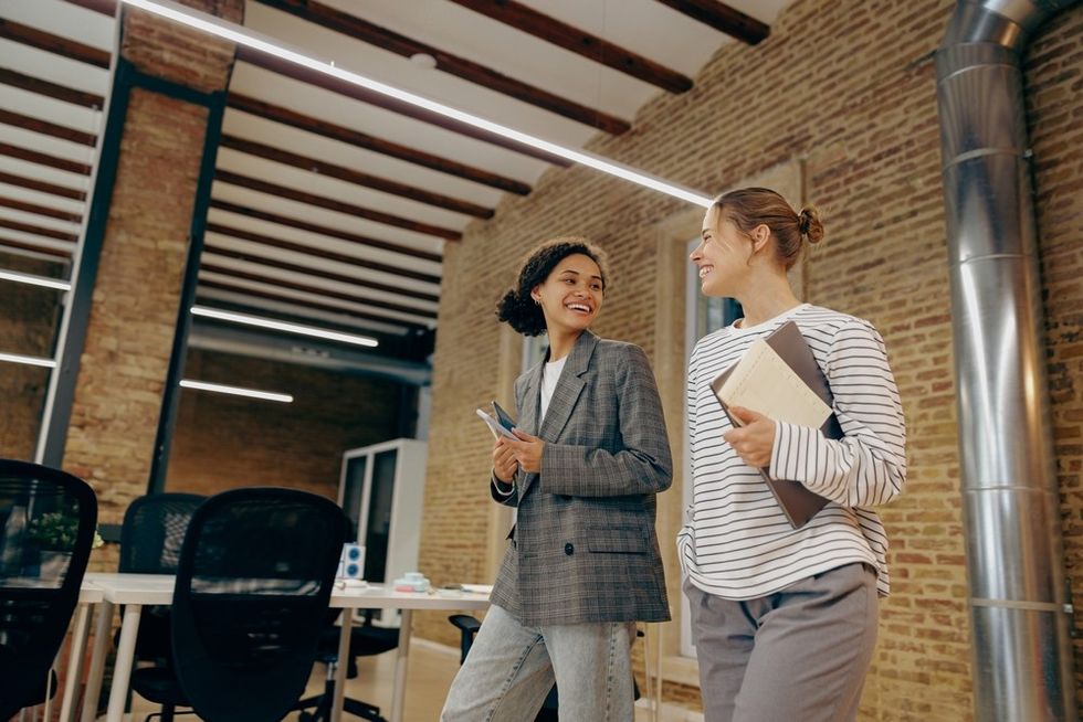 Two women chatting and walking in a modern office with exposed brick walls.