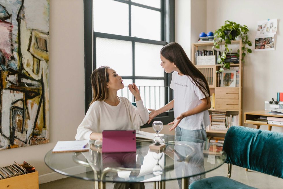 Two women discuss in a cozy office setting with art and plants.