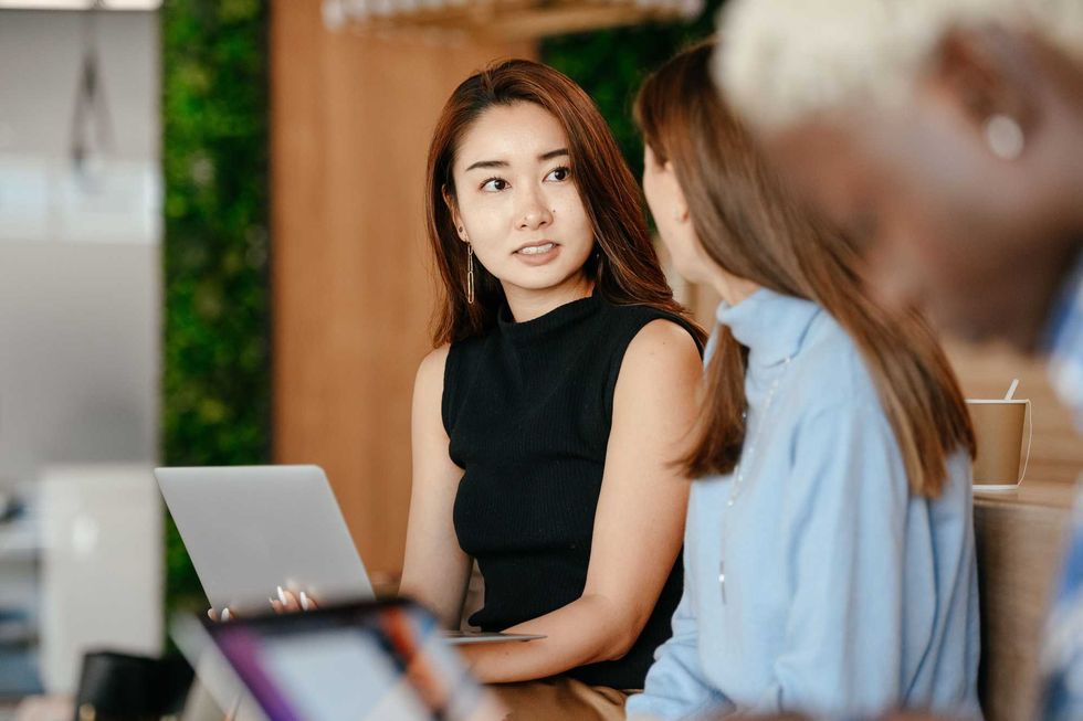 Two women discussing in an office setting, one holding a laptop.
