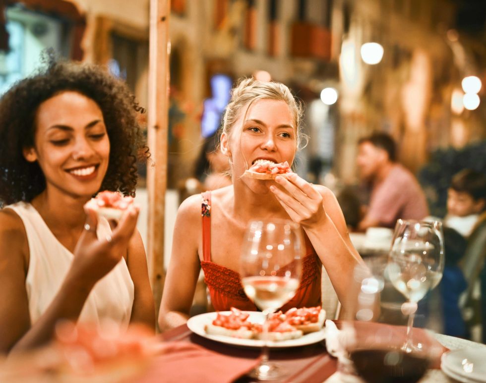 Two women enjoying bruschetta at a lively outdoor restaurant.