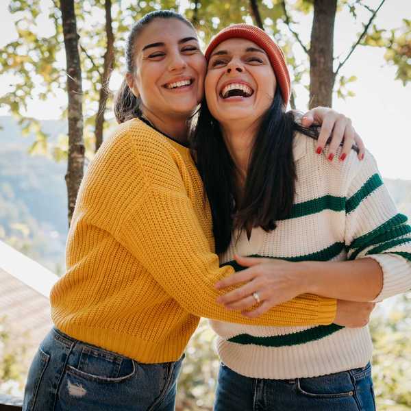Two women hugging and laughing outdoors on a sunny day.