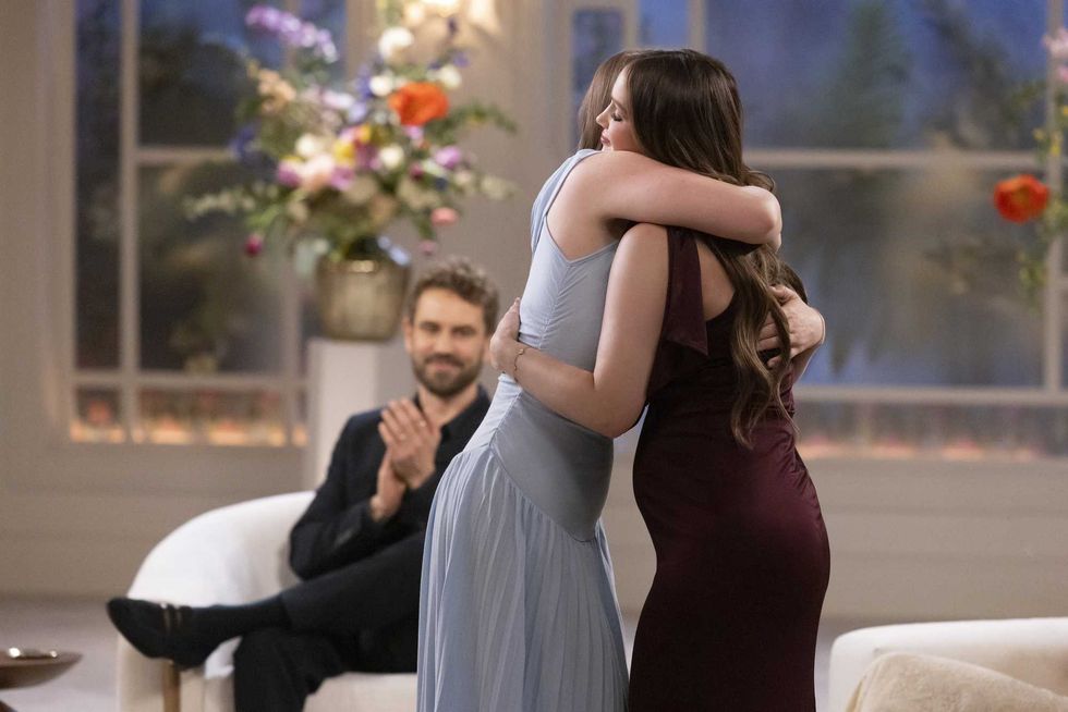 Two women hugging at a rose ceremony, while a man claps in the background.