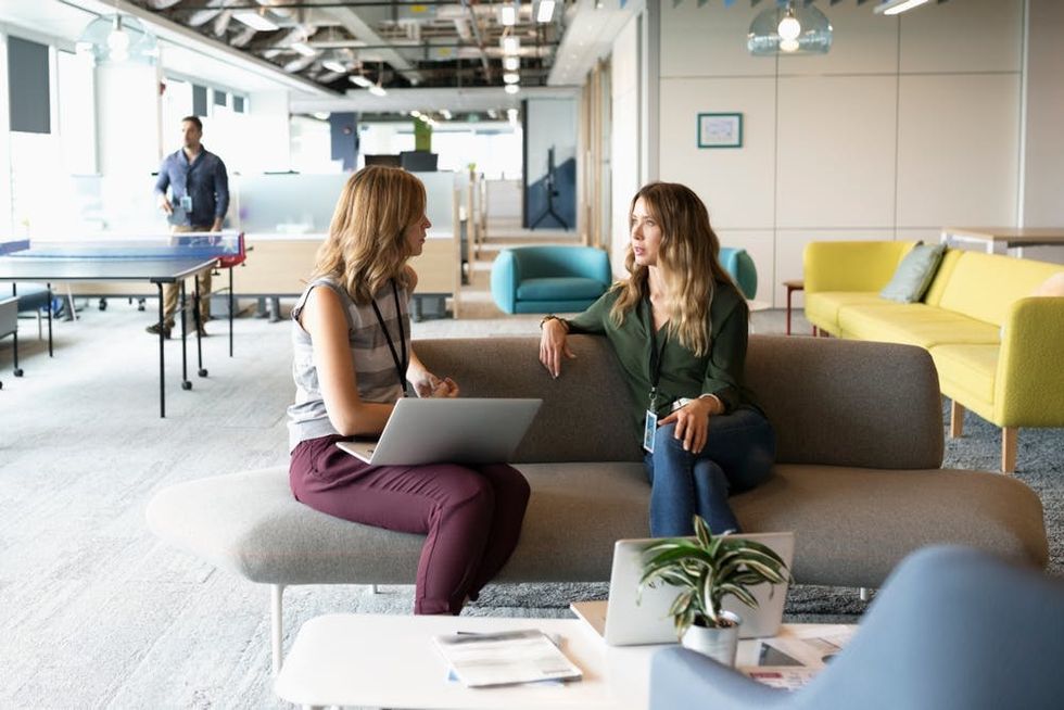 Two women in an office have a conversation on a sofa