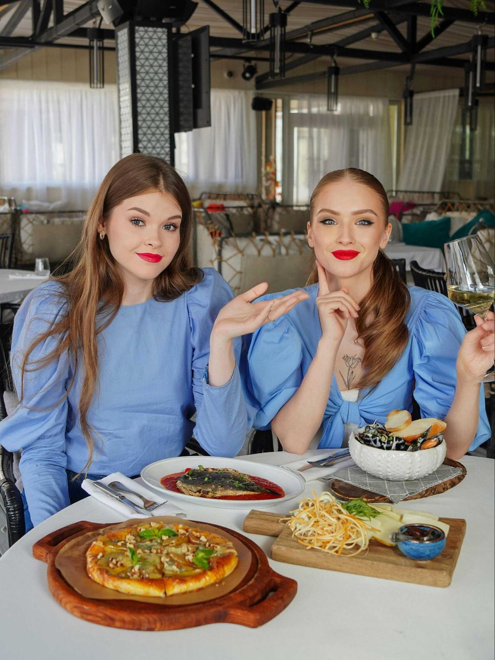 Two women in blue outfits dining with pizza and seafood dishes.