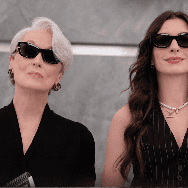 Two women in sunglasses, wearing black outfits, standing confidently indoors.