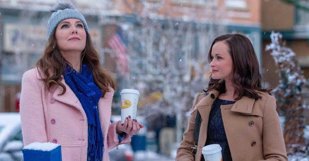 Two women in winter coats, holding coffee cups, standing in a snowy street.