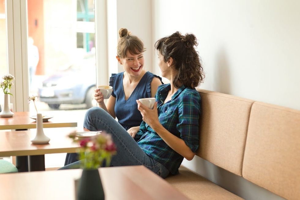 Two women laugh together inside a coffee shop