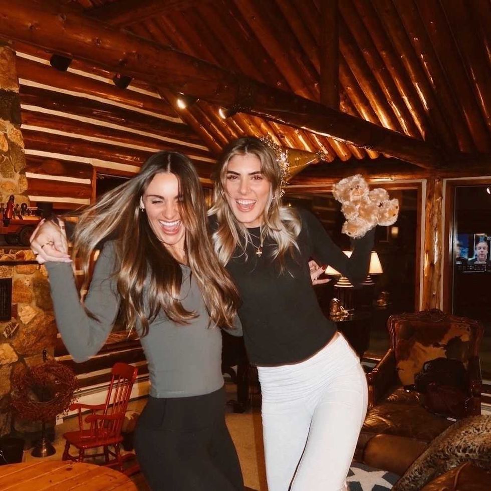 Two women laughing and dancing in a cozy log cabin room.