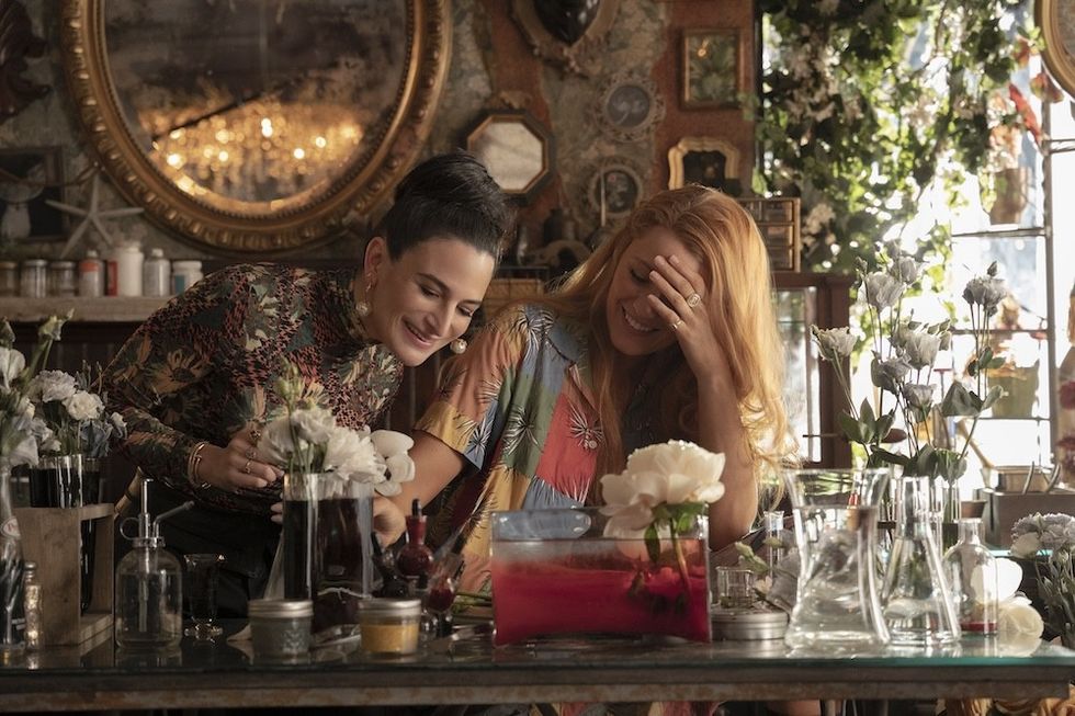 Two women laughing together in a flower-filled workshop.