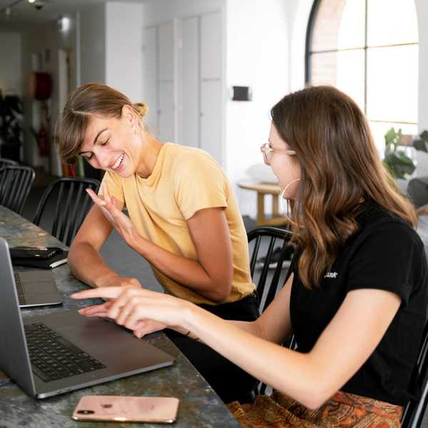 Two women laughing while discussing something on a laptop.