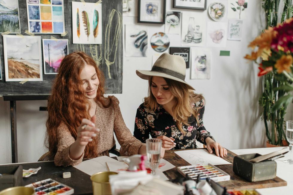 Two women painting in an art studio, surrounded by colorful artworks.