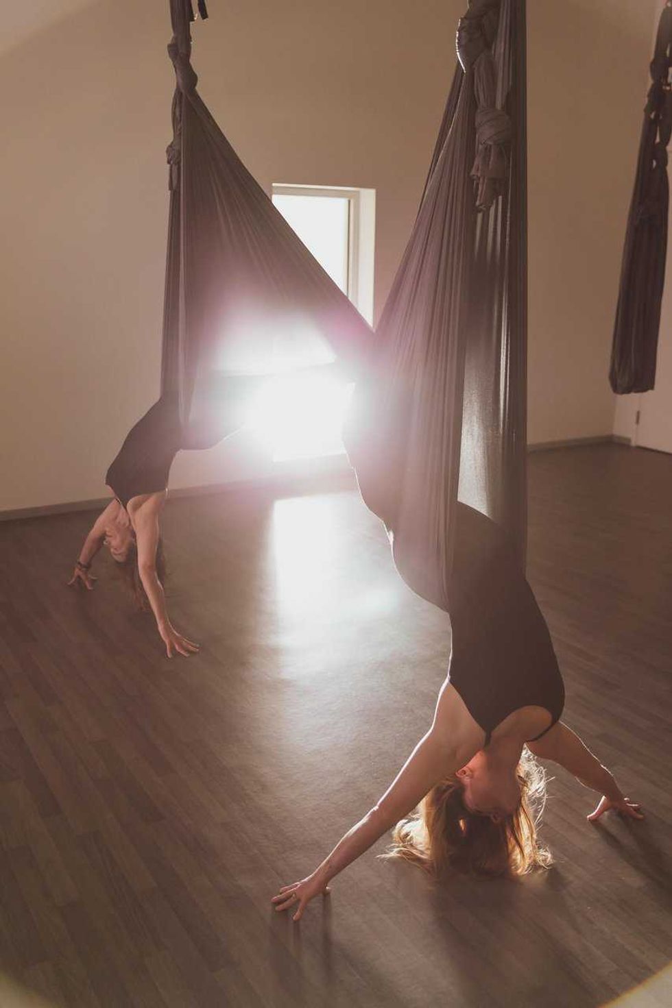 Two women performing aerial yoga, suspended upside down in fabric hammocks.