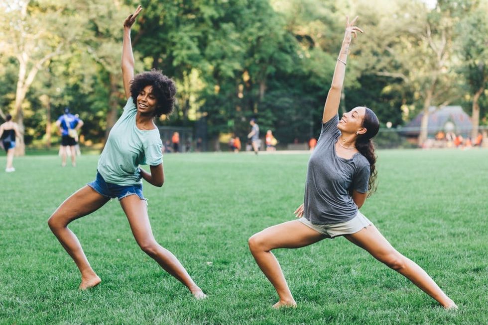 Two women practice yoga poses together in a park