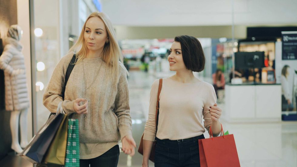 Two women shopping, carrying bags and talking in a mall.