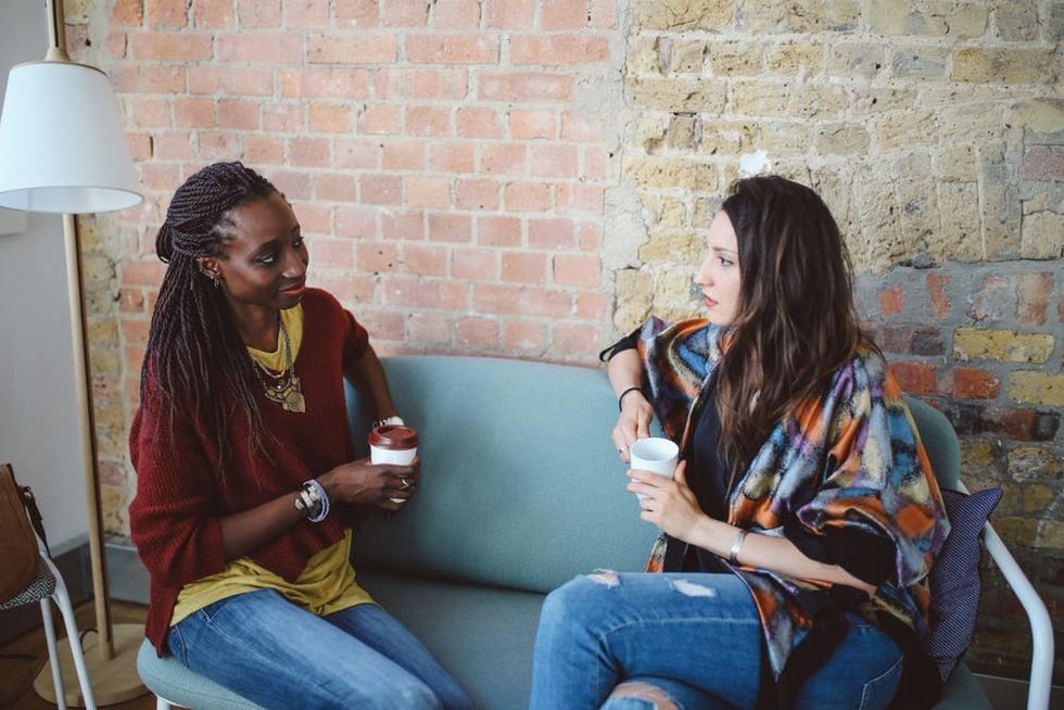 Two women sit on a sofa talking to each other
