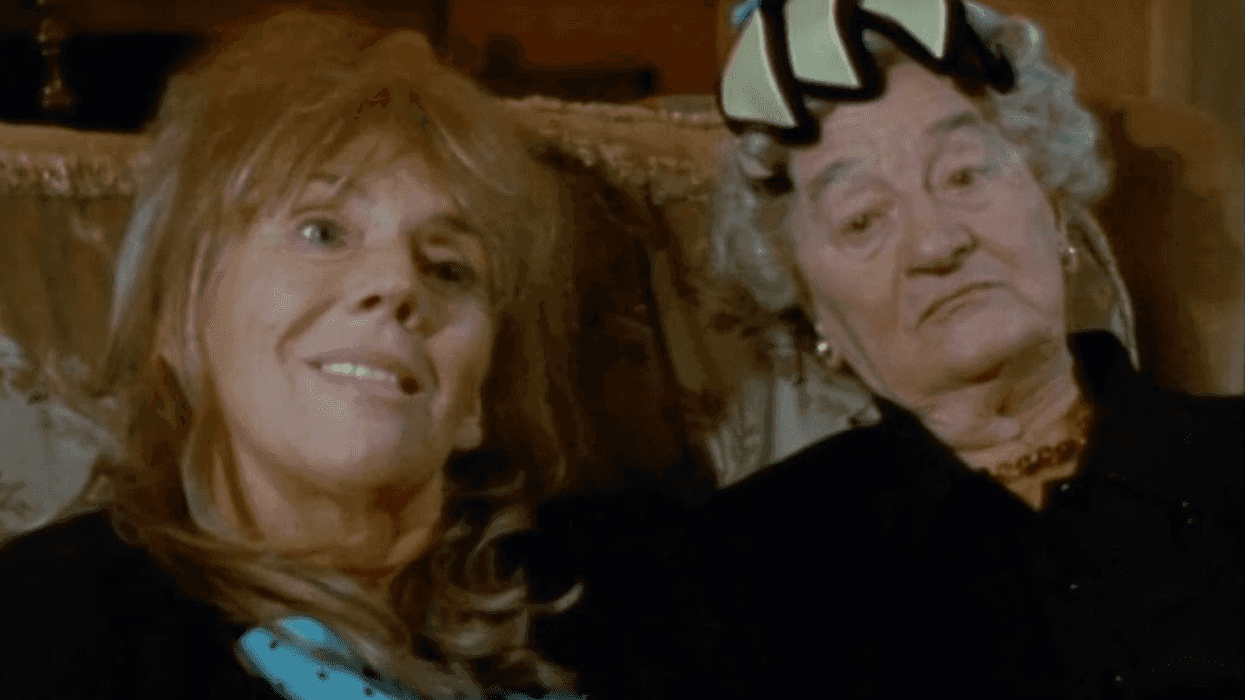 Two women sitting on a couch, one smiling, the other wearing a hat with a neutral expression.