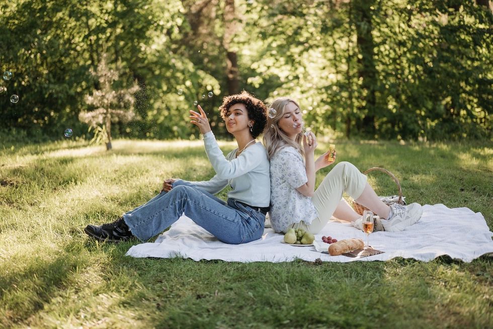 two women sitting on a picnic blanket blowing bubbles