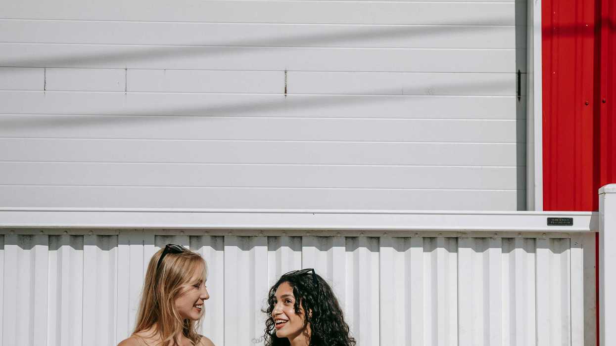 Two women smiling and chatting by a red and white wall.