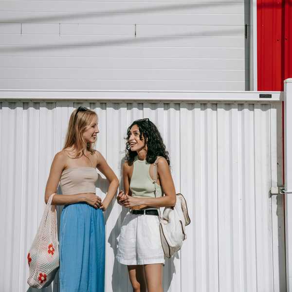 Two women smiling and chatting by a red and white wall.