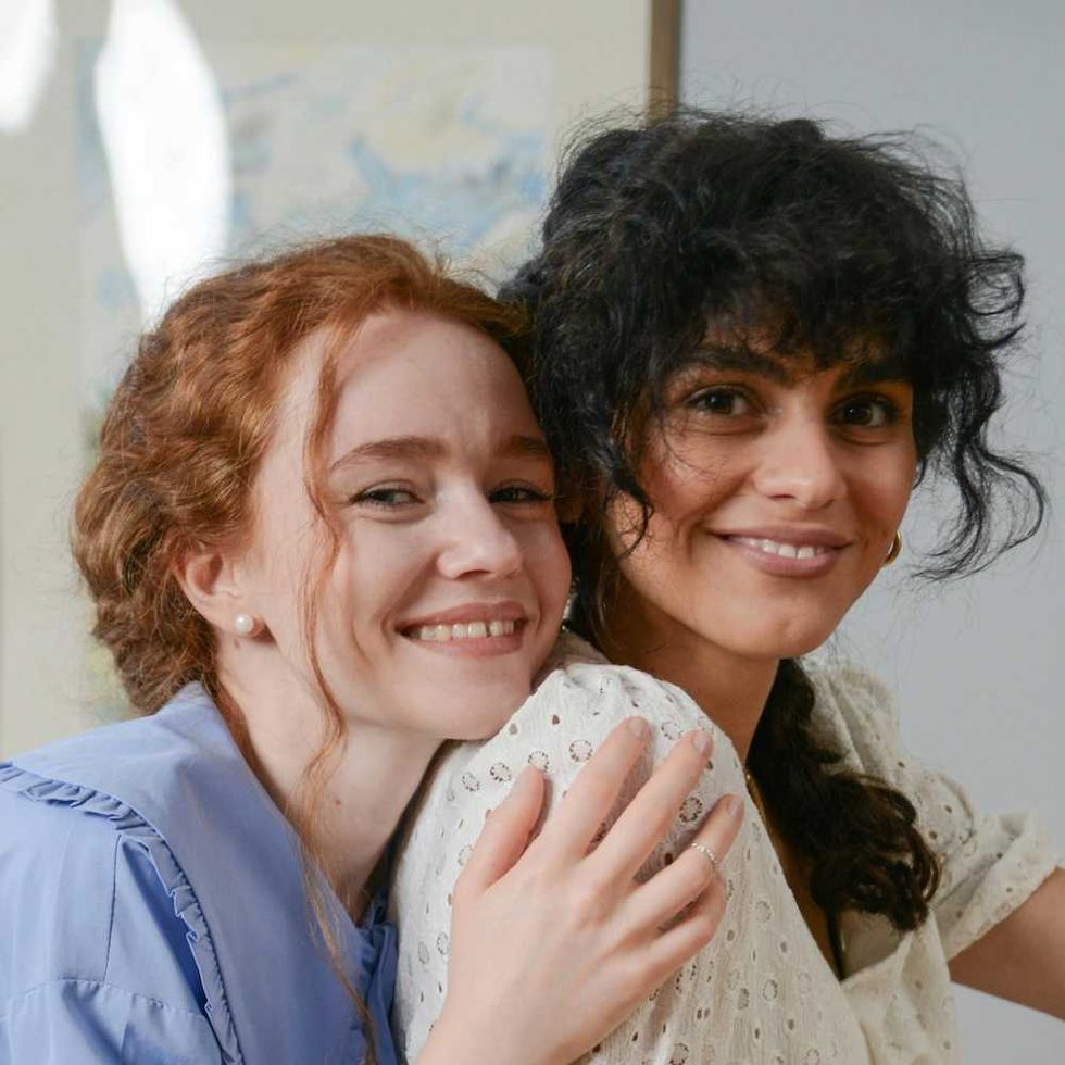 Two women smiling and hugging closely indoors.