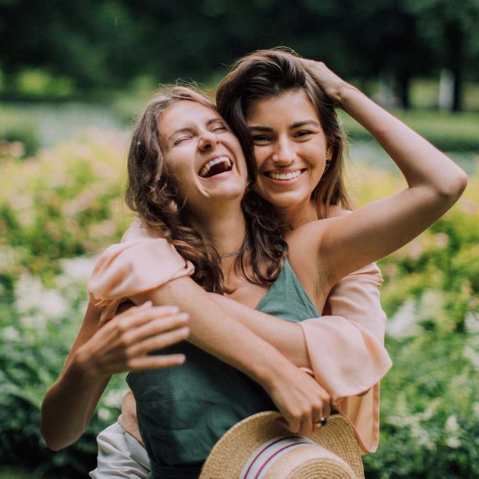 Two women smiling and hugging in a sunny, green park.