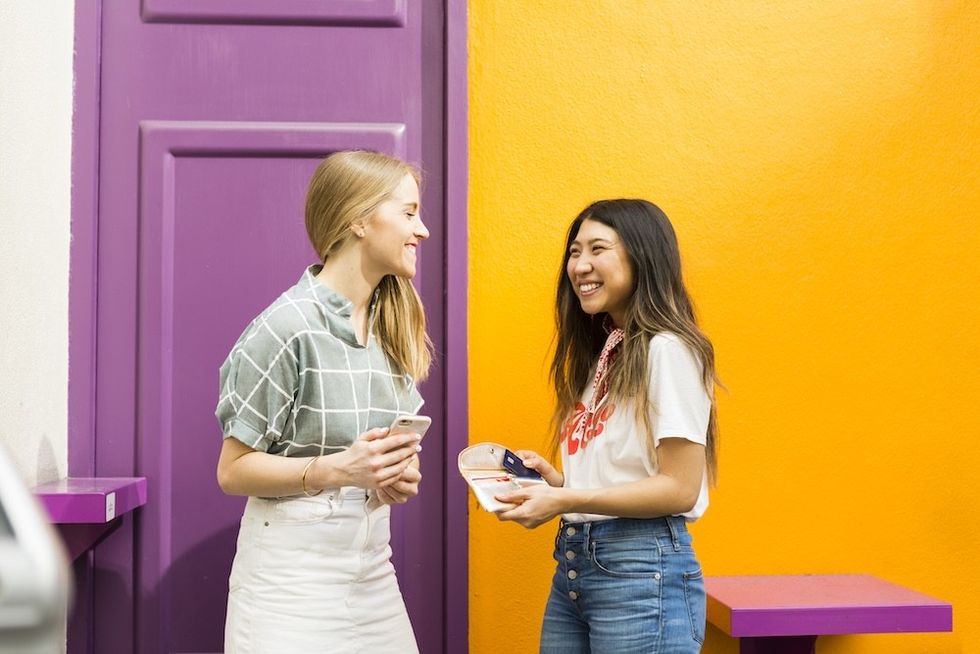 two women standing against a colorful wall