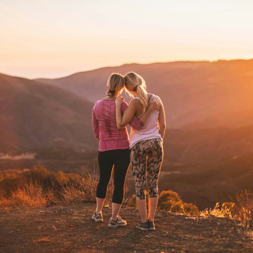 two women standing side by side, looking at the sunset in the mountains