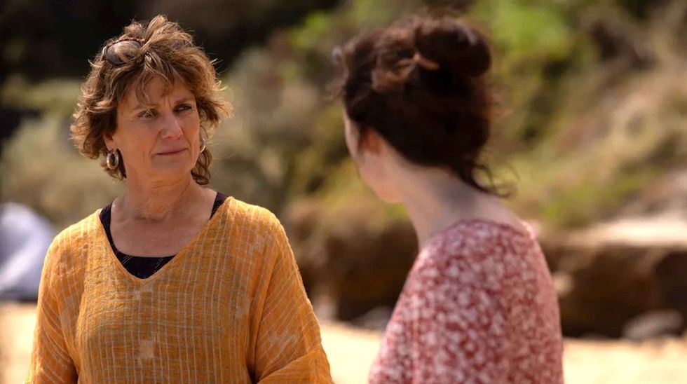 Two women talking outdoors, one in orange, the other in red floral.