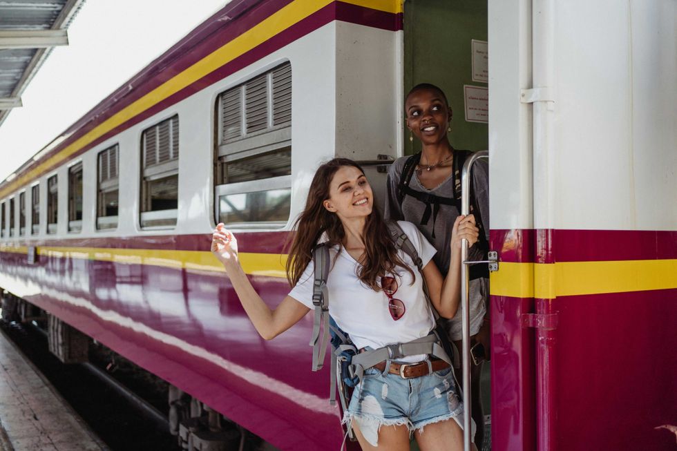 Two women with backpacks smiling while stepping out of a colorful train.