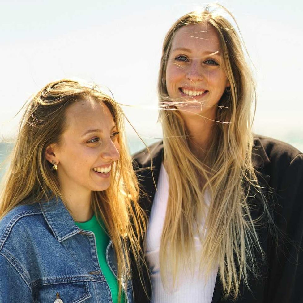 Two women with long blonde hair smiling outdoors on a sunny day.
