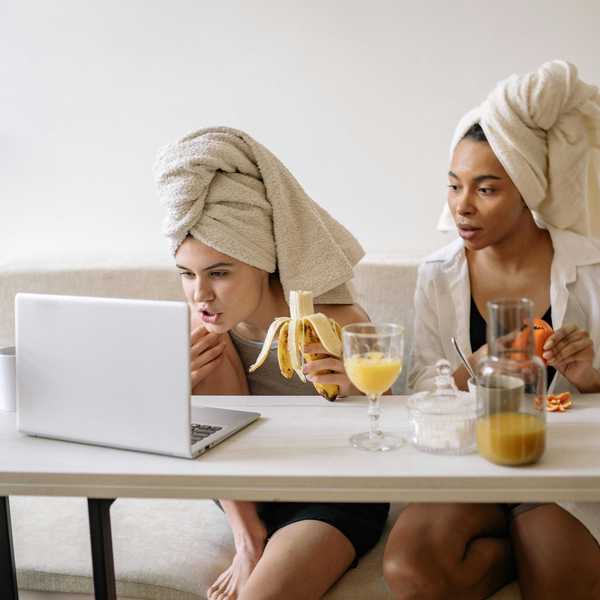 Two women with towel turbans eating and watching a laptop at a table.