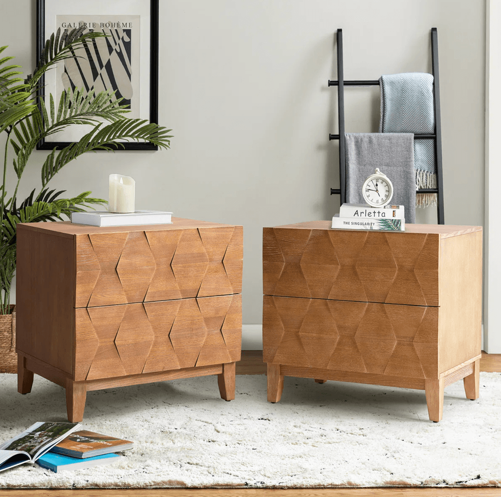 Two wooden geometric nightstands on a rug, with decor, plants, and a ladder rack.