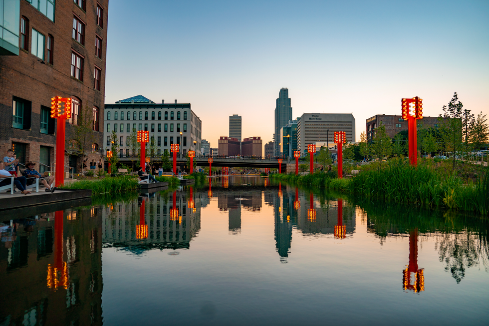 Urban canal at dusk with lit orange lanterns and city skyline reflection in water.